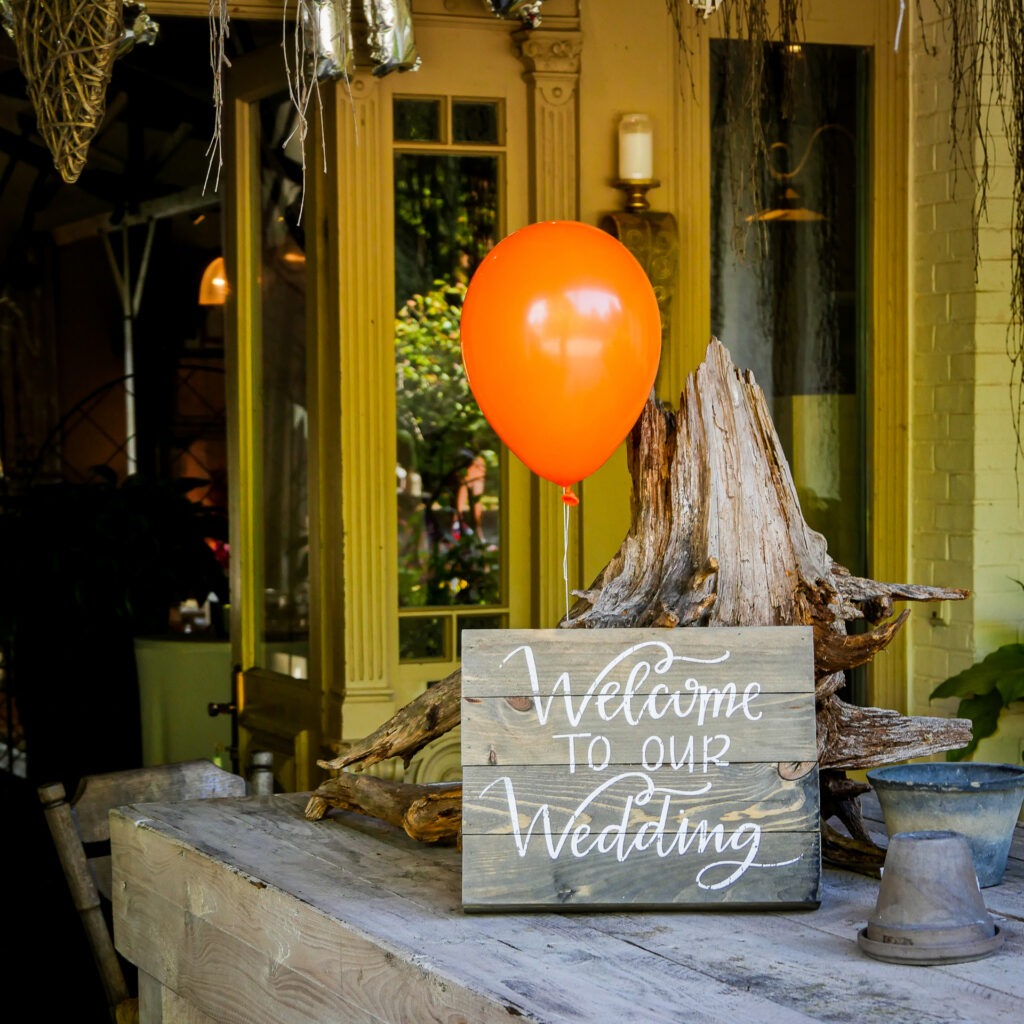 Holzschild mit der Aufschrift „Welcome to our Wedding“ und rotem Ballon als Hochzeitsdeko